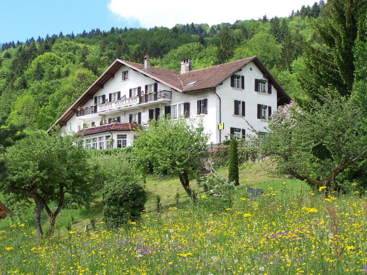 une grande maison blanche sur une colline avec un champ de fleurs dans l'établissement Hôtel Restaurant Taillard, à Goumois