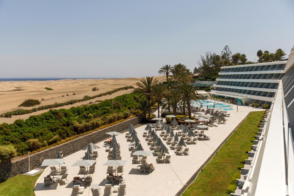 una fila de sillas y sombrillas junto a un edificio en Santa Monica Suites Hotel, en Playa del Inglés