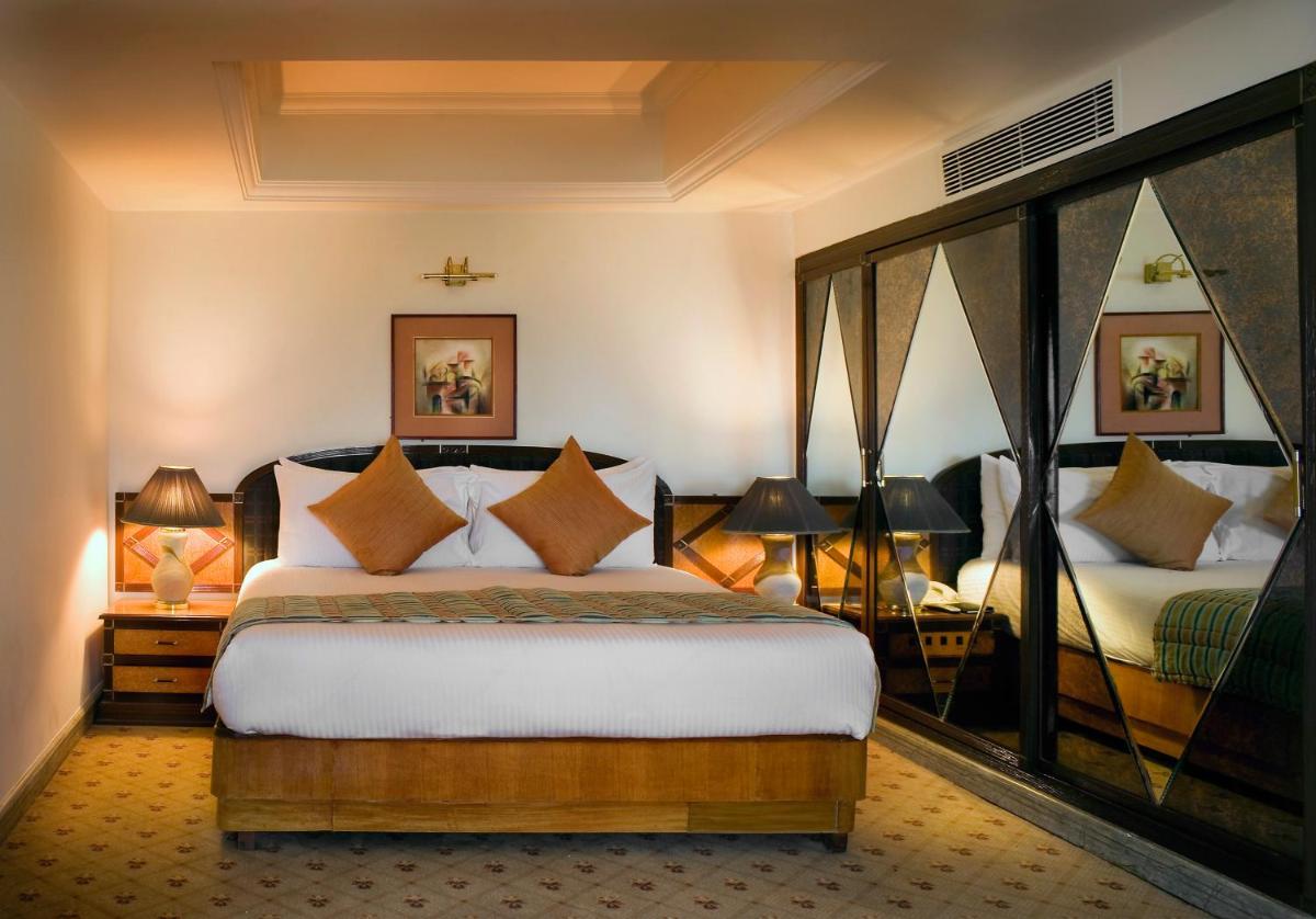 a bedroom with a bed and two lamps and two beds at The Suryaa New Delhi in New Delhi a bedroom with a bed and two lamps and two beds at The Suryaa New Delhi in New Delhi