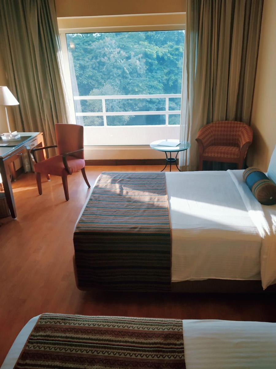 a hotel room with a bed and a large window at The Lalit Ashok in Bengaluru a hotel room with a bed and a large window at The Lalit Ashok in Bengaluru