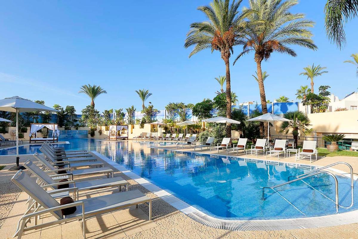 Una gran piscina con tumbonas y palmeras. en Exe Estepona Thalasso & Spa- Adults Only, en Estepona