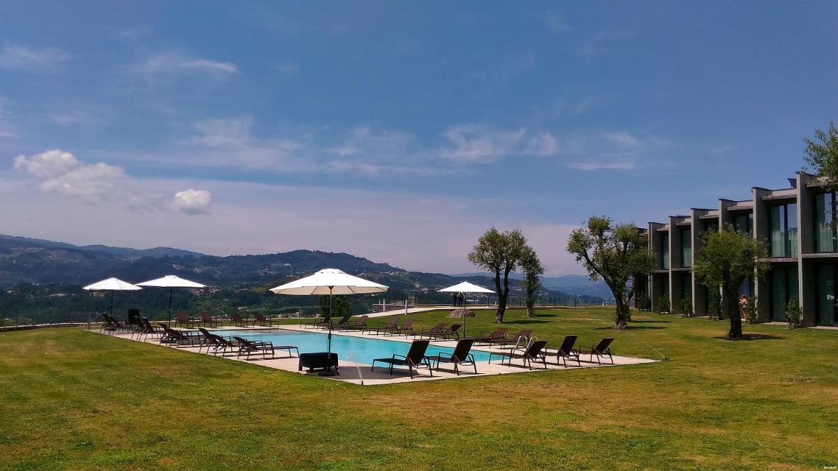 uma piscina com cadeiras e guarda-sóis ao lado de um prédio em Tempus Hotel & Spa em Ponte da Barca