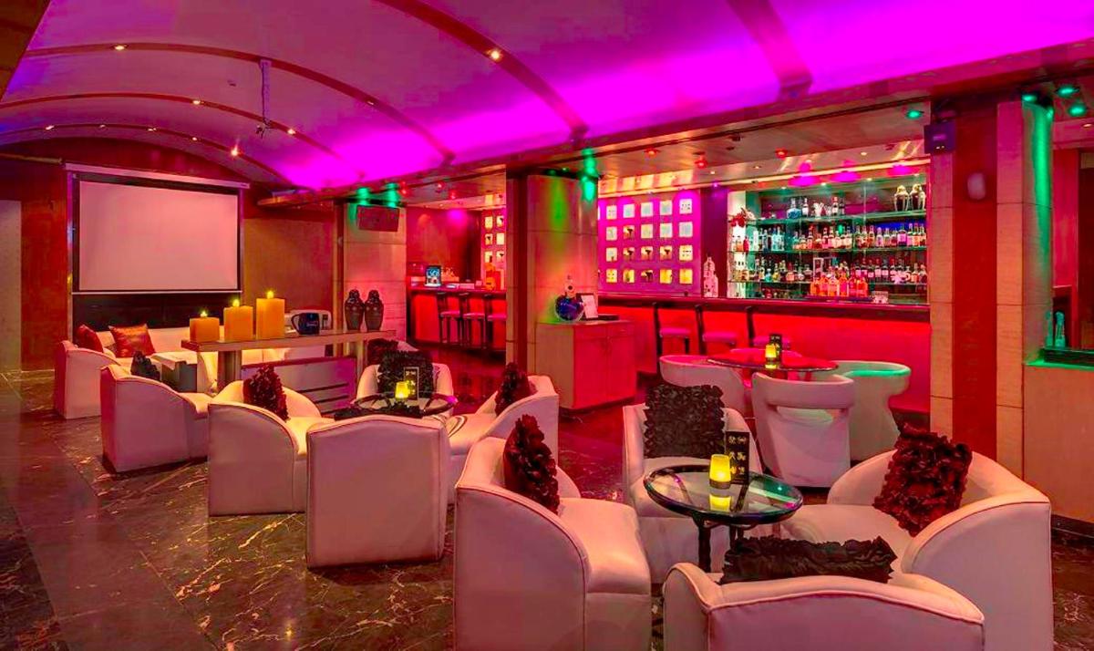 a room with white chairs and a bar with purple lighting at Hotel Hindusthan International, Kolkata in Kolkata