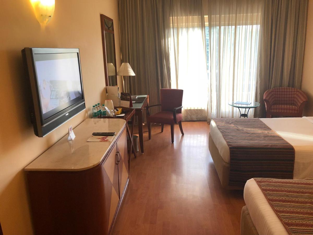a hotel room with a bed and a flat screen tv at The Lalit Ashok in Bengaluru a hotel room with a bed and a flat screen tv at The Lalit Ashok in Bengaluru