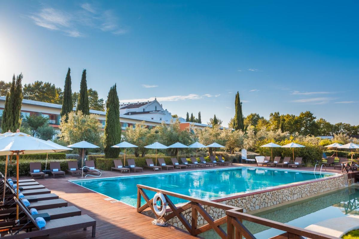 uma piscina de hotel com cadeiras e guarda-sóis em Convento do Espinheiro, Historic Hotel & Spa em Évora