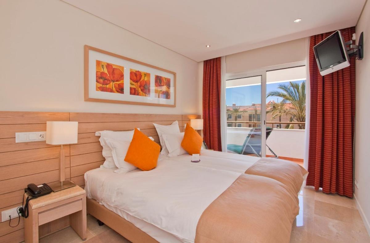 um quarto com uma cama com almofadas laranja e uma janela em As Cascatas Golf Resort & Spa em Vilamoura
