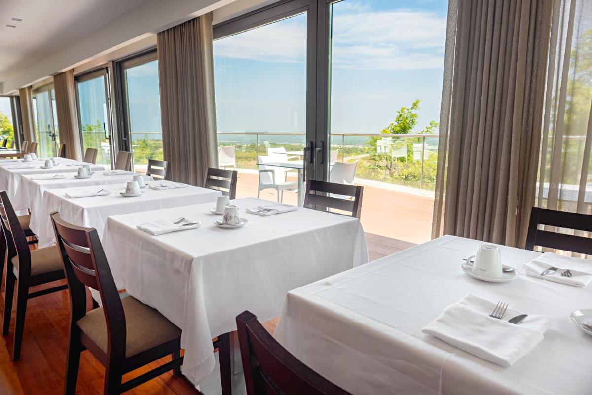 um restaurante com mesas e cadeiras brancas e uma grande janela em Hotel dos Zimbros em Sesimbra