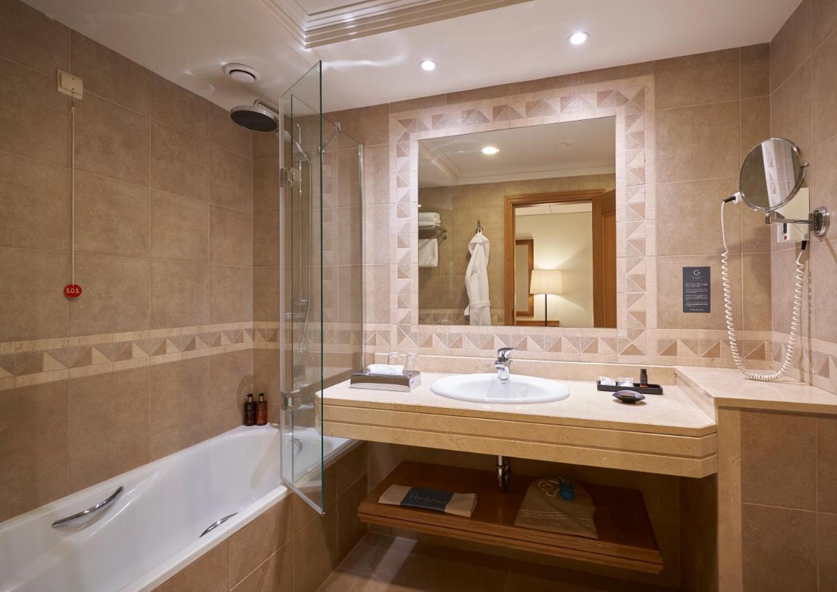 um banheiro com uma pia, uma banheira e um espelho em Hotel Porto Mare - PortoBay no Funchal