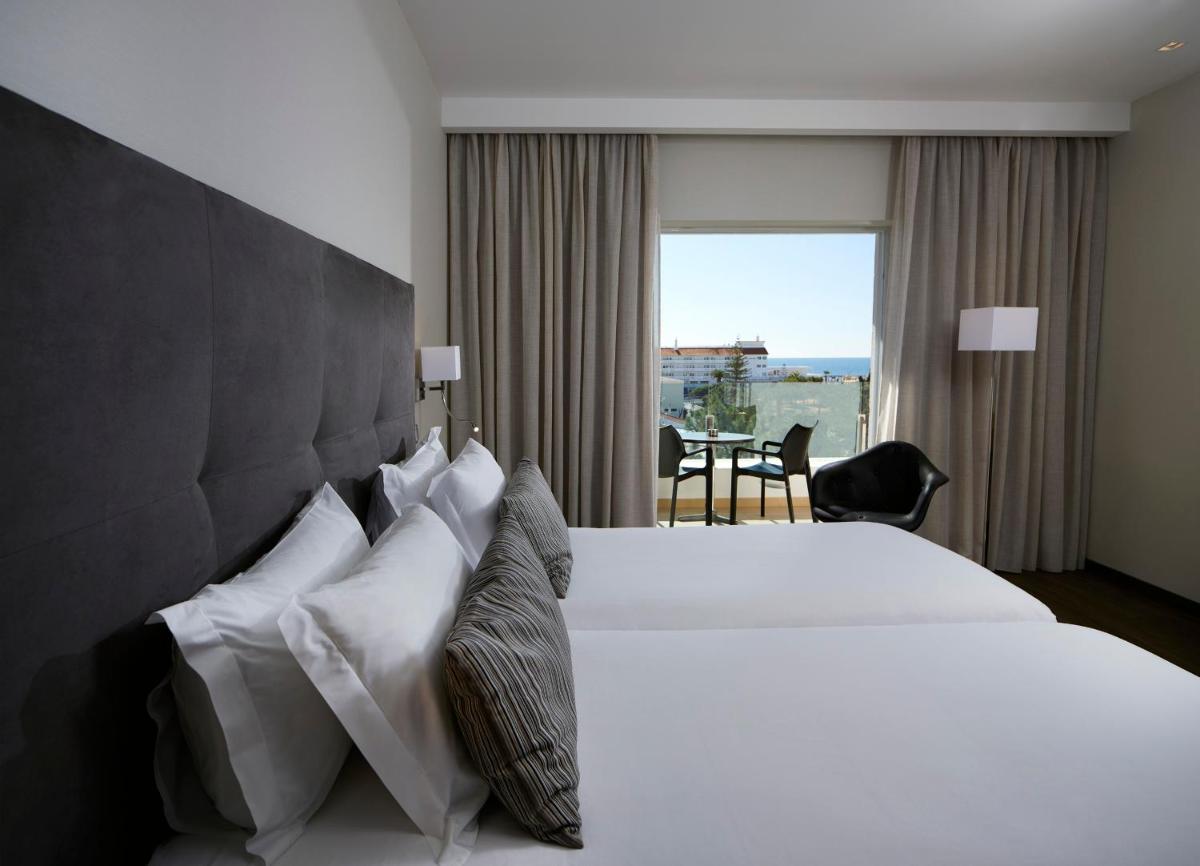 um quarto de hotel com uma grande cama branca e uma janela em Alcazar Hotel & SPA em Monte Gordo