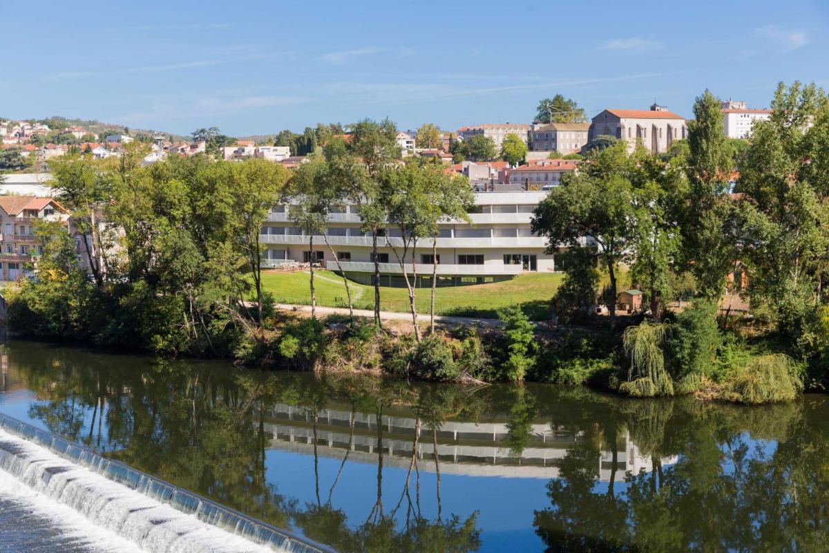 un bâtiment au bord d'une rivière avec des arbres dans l'établissement Best Western Plus Hotel Divona Cahors, à Cahors