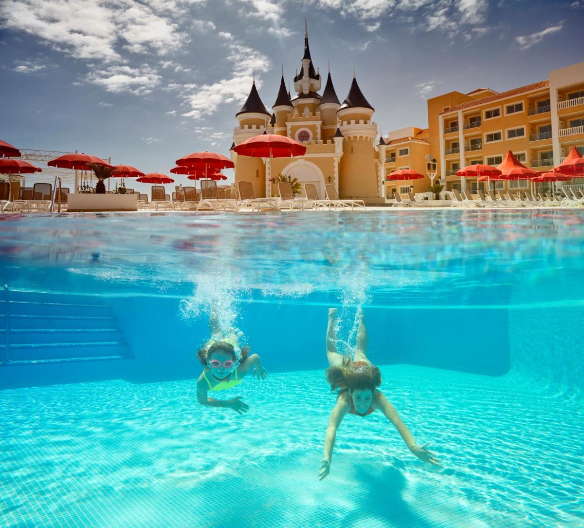 Dos personas nadando en una piscina frente a un hotel en Bahia Principe Fantasia Tenerife - All Inclusive, en San Miguel de Abona