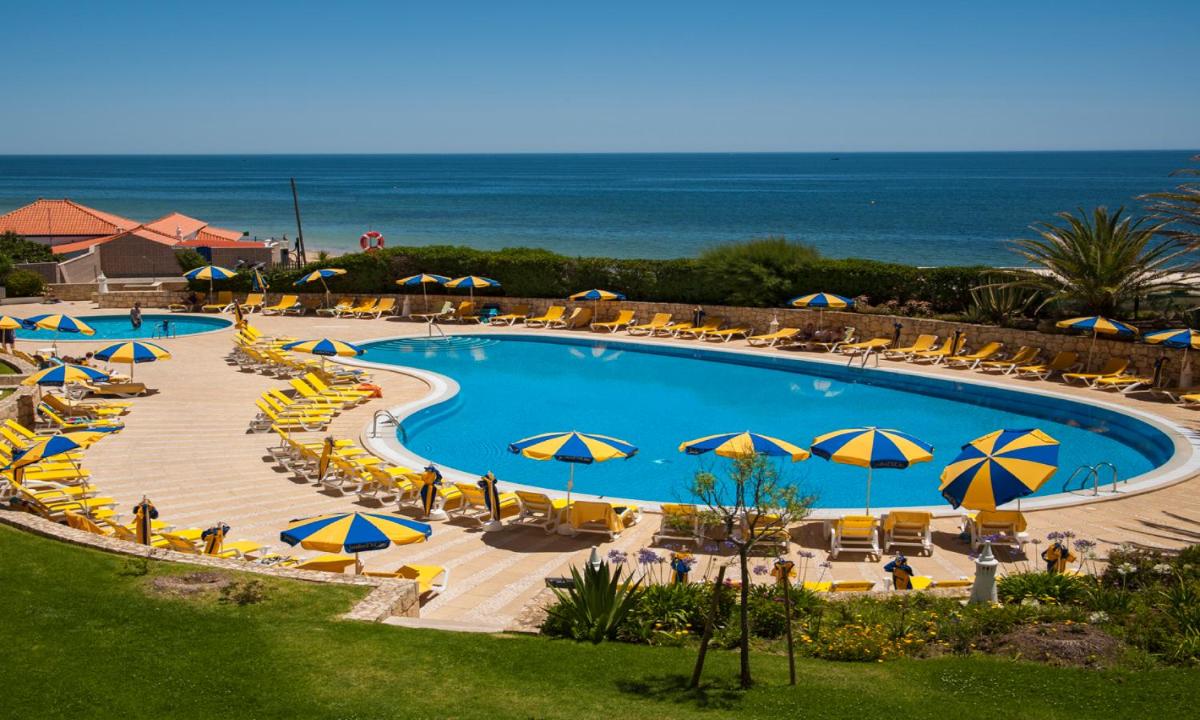 uma piscina com guarda-sóis e cadeiras e o oceano em Jardim do Vau em Portimão