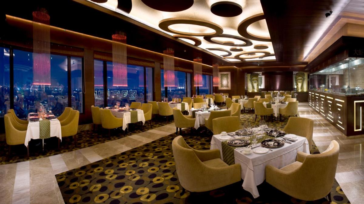 a restaurant with white tables and yellow chairs and windows at The Suryaa New Delhi in New Delhi a restaurant with white tables and yellow chairs and windows at The Suryaa New Delhi in New Delhi
