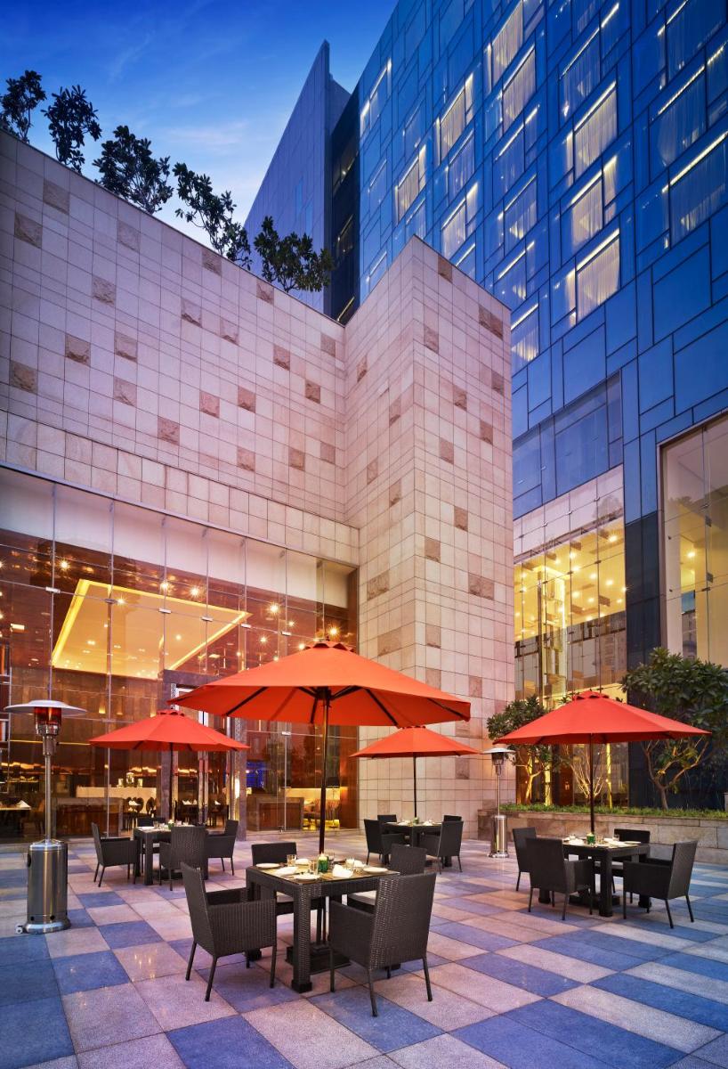 a restaurant with tables and umbrellas in front of a building at Taj City Centre Gurugram in Gurgaon