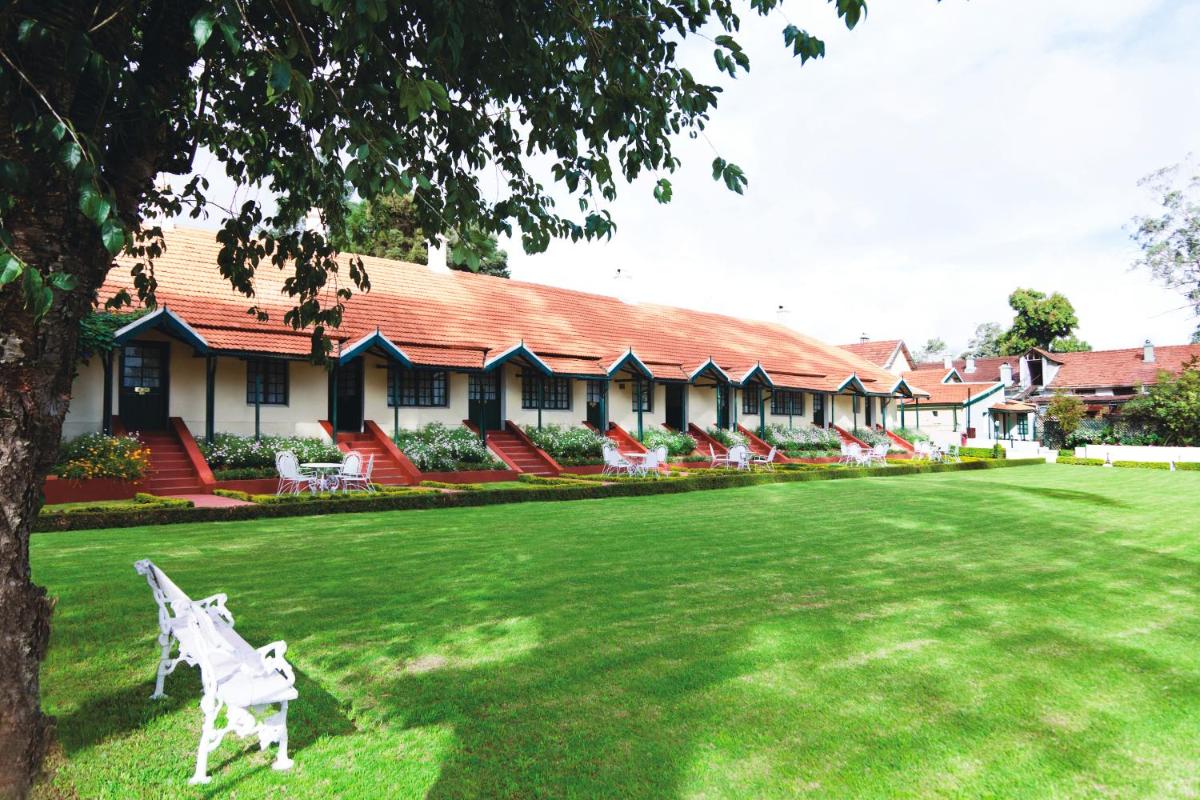 a white bench sitting in the grass in front of a building at Savoy - IHCL SeleQtions in Ooty