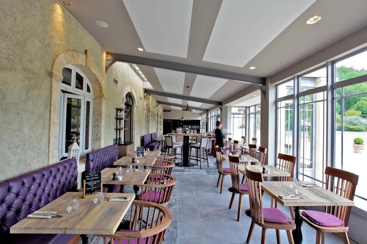 un restaurant avec des tables et des chaises en bois et des fenêtres dans l'établissement Les Glycines - Hôtel & Spa - Teritoria, à Les Eyzies-de-Tayac
