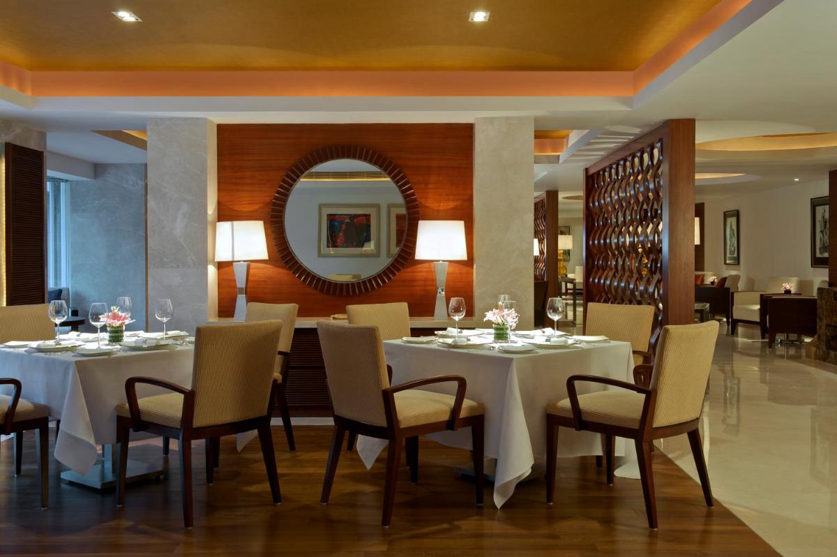 a dining room with white tables and chairs and a mirror at Taj Coromandel in Chennai