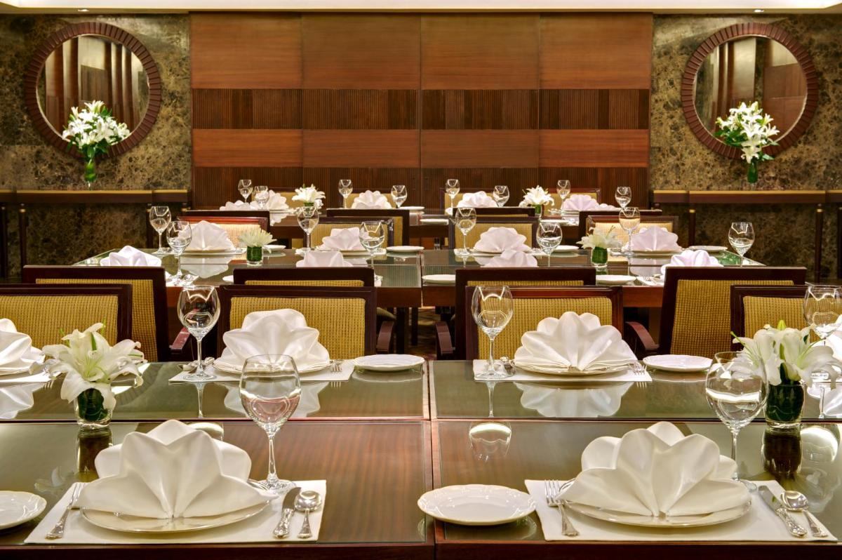 a dining room with tables and chairs with white dishes at Taj Coromandel in Chennai