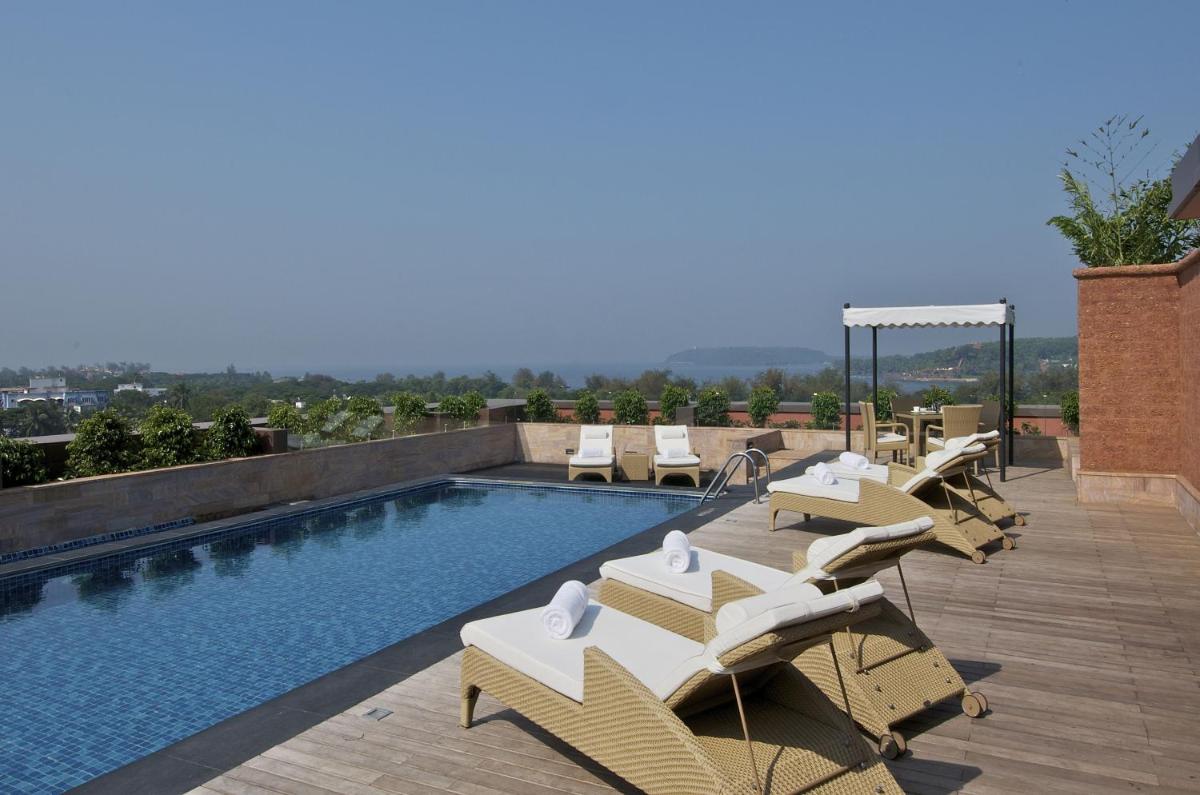 a swimming pool with white lounge chairs on a roof at Vivanta Goa, Panaji in Panaji a swimming pool with white lounge chairs on a roof at Vivanta Goa, Panaji in Panaji