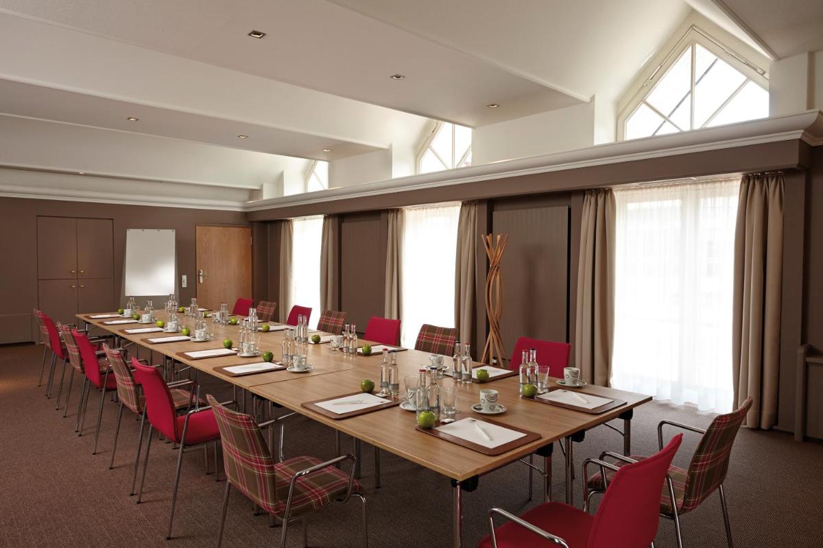 ein großer Konferenzraum mit einem langen Tisch und roten Stühlen in der Unterkunft Aalernhüs hotel & spa in Sankt Peter-Ording + 37 Fotos