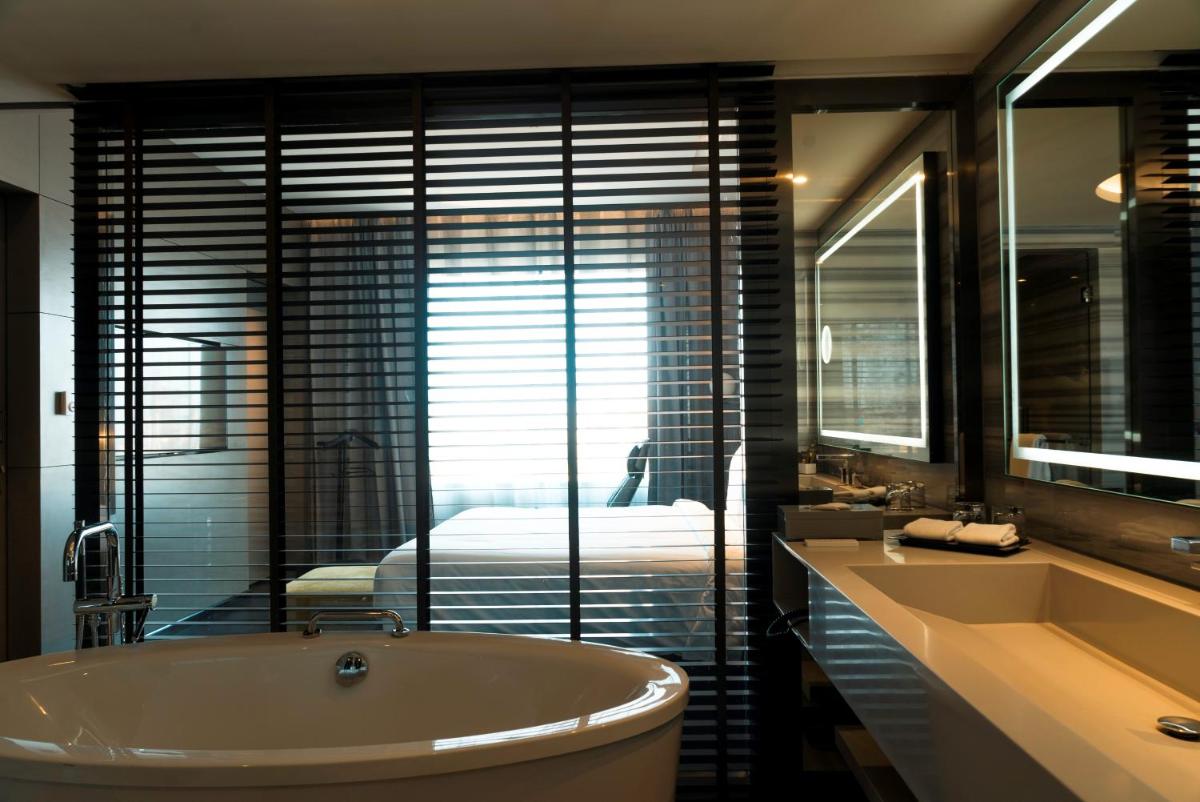 a bathroom with a tub and a sink and a bed at Novotel Chennai Chamiers Road in Chennai