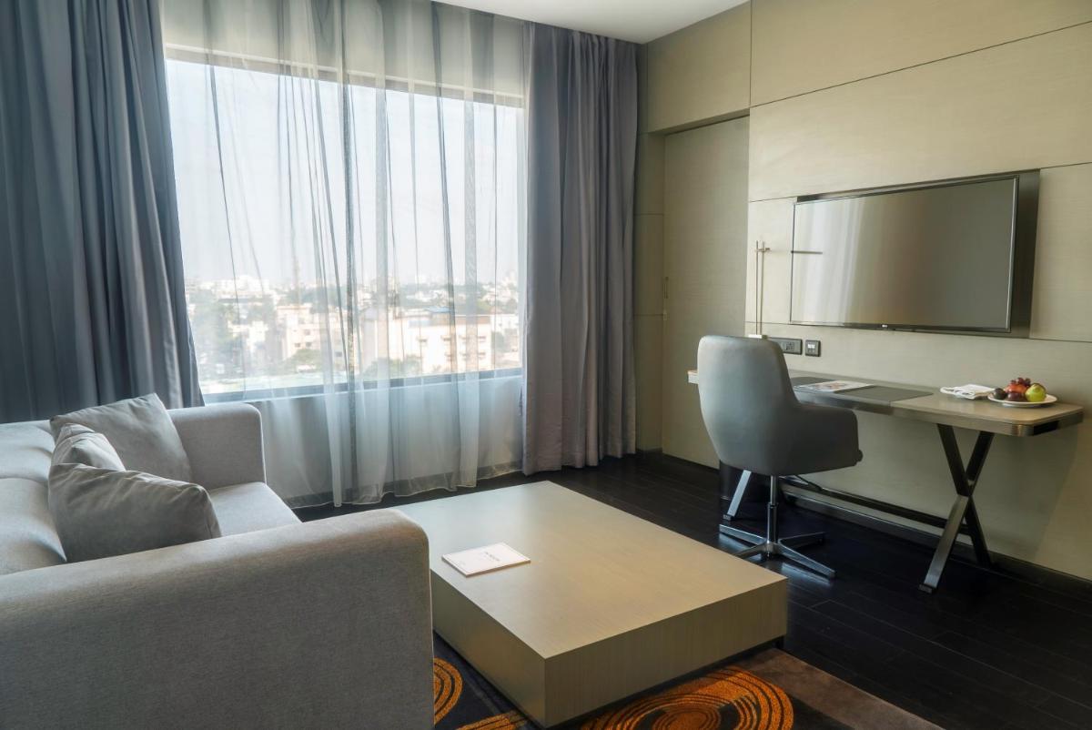 a hotel room with a couch and a desk and a window at Novotel Chennai Chamiers Road in Chennai