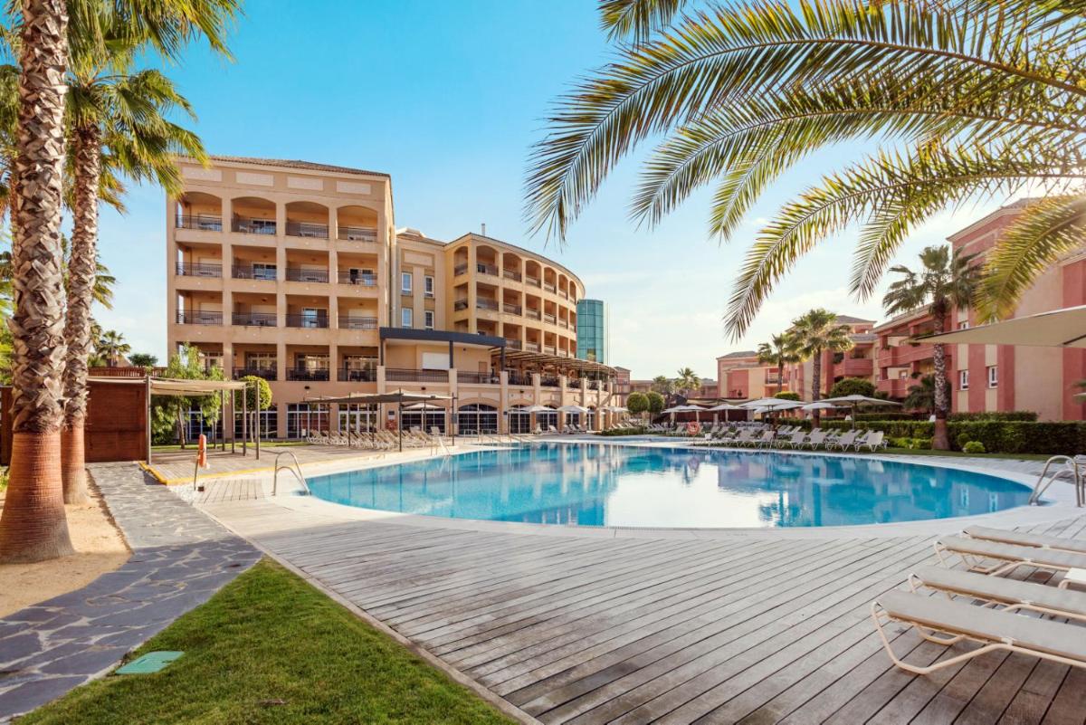 una piscina con palmeras y edificios en Ama Islantilla Resort, en Islantilla