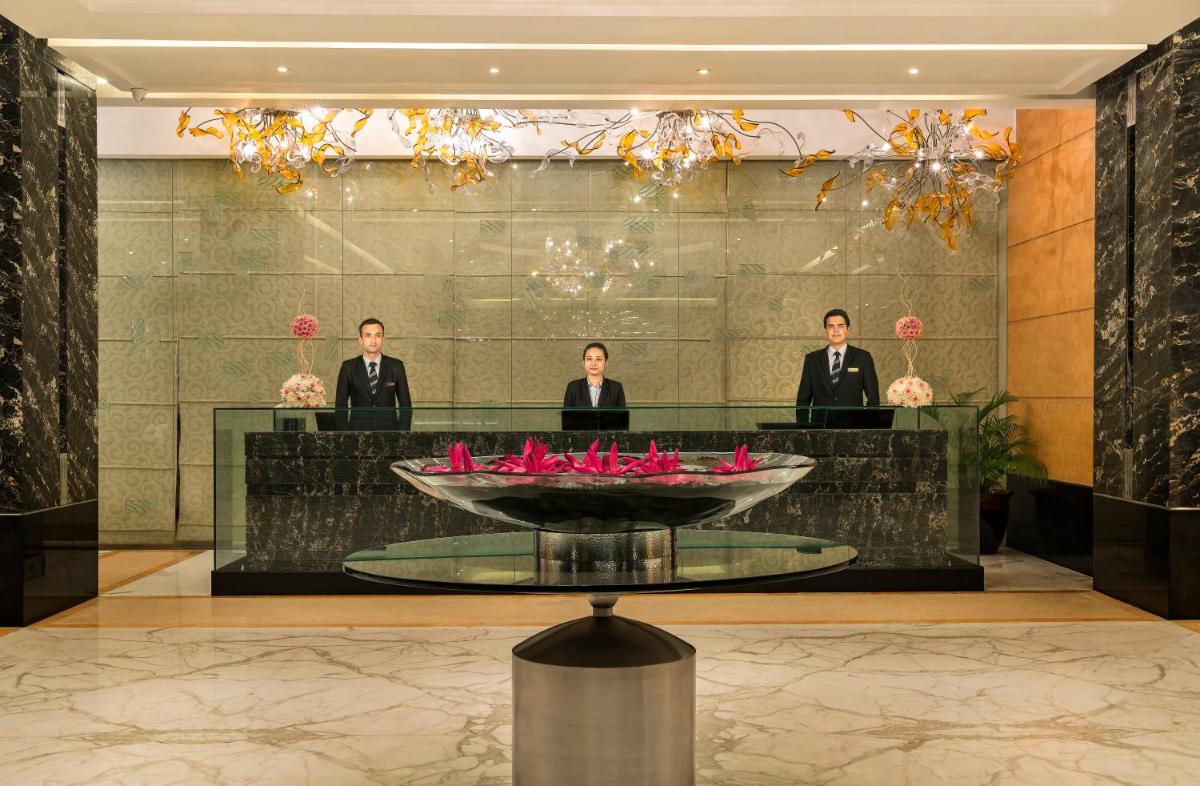 three people in a lobby with a table with pink flowers at Taj Club House in Chennai