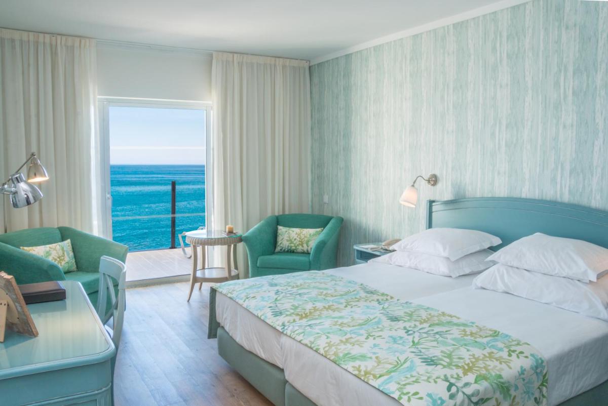 um quarto com uma cama e cadeiras e uma grande janela em Pestana Madeira Beach Club no Funchal