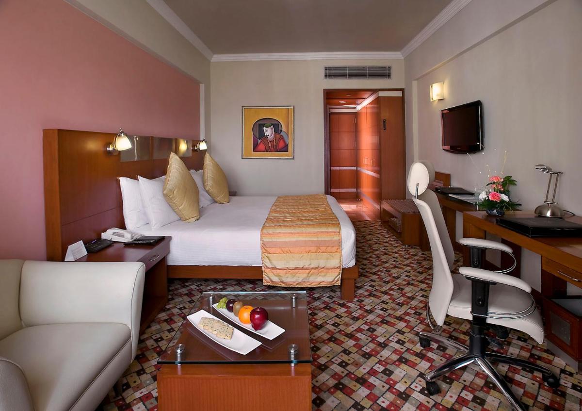 a hotel room with a bed and a desk at The Suryaa New Delhi in New Delhi a hotel room with a bed and a desk at The Suryaa New Delhi in New Delhi
