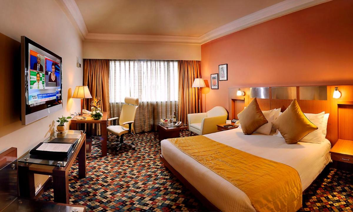 a hotel room with a bed and a living room at The Suryaa New Delhi in New Delhi a hotel room with a bed and a living room at The Suryaa New Delhi in New Delhi