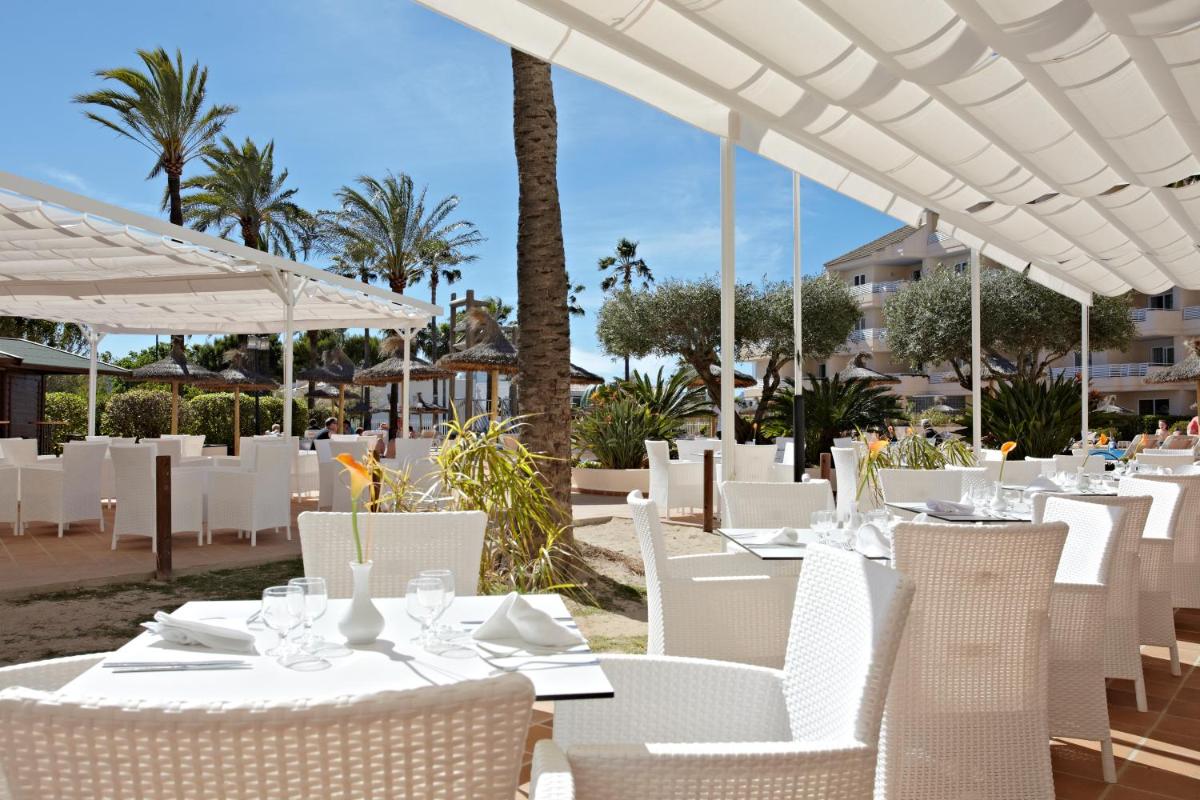 un restaurante con mesas blancas y sillas blancas en Grupotel Port D´Alcudia, en Puerto de Alcudia