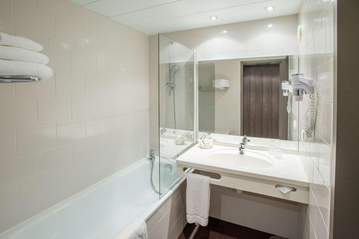 une salle de bain avec un lavabo, une baignoire et un miroir dans l'établissement Best Western Plus Hotel Admiral, à La Tour-de-Salvagny