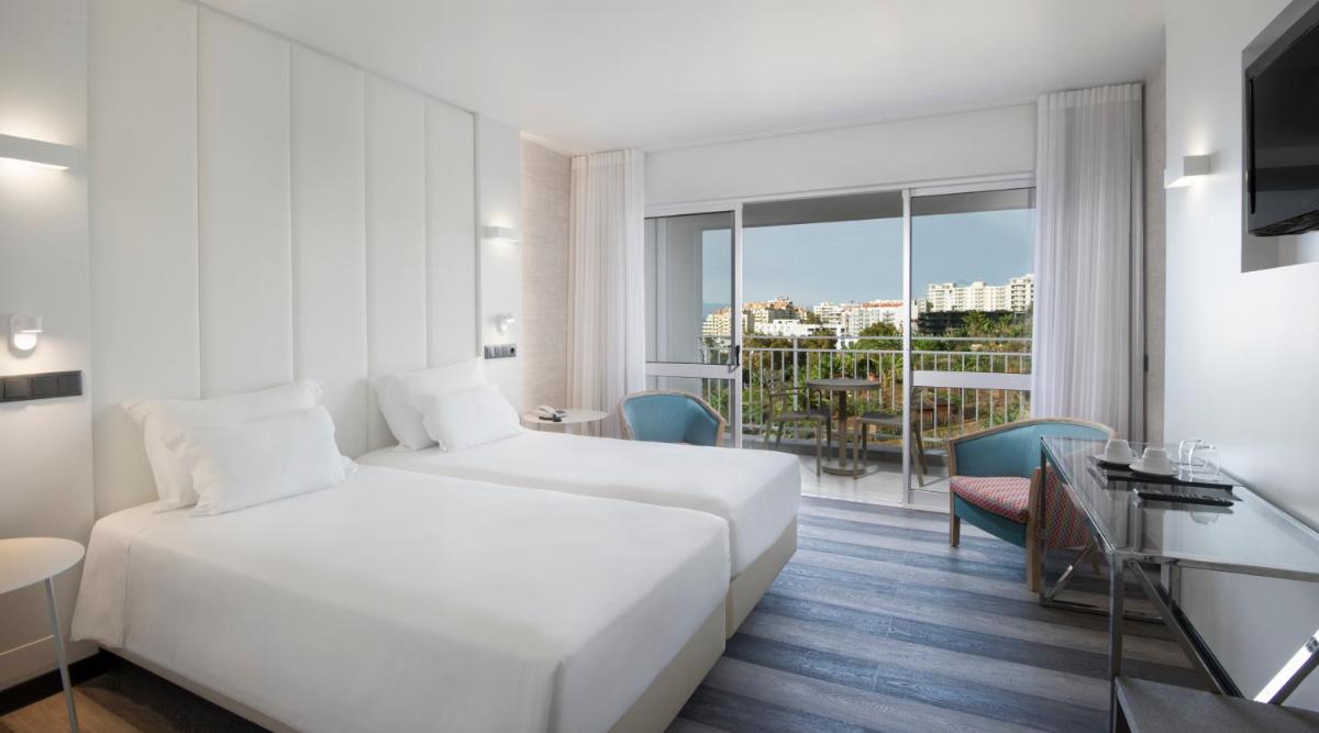 um quarto de hotel com uma cama branca e uma varanda em Hotel Alto Lido no Funchal