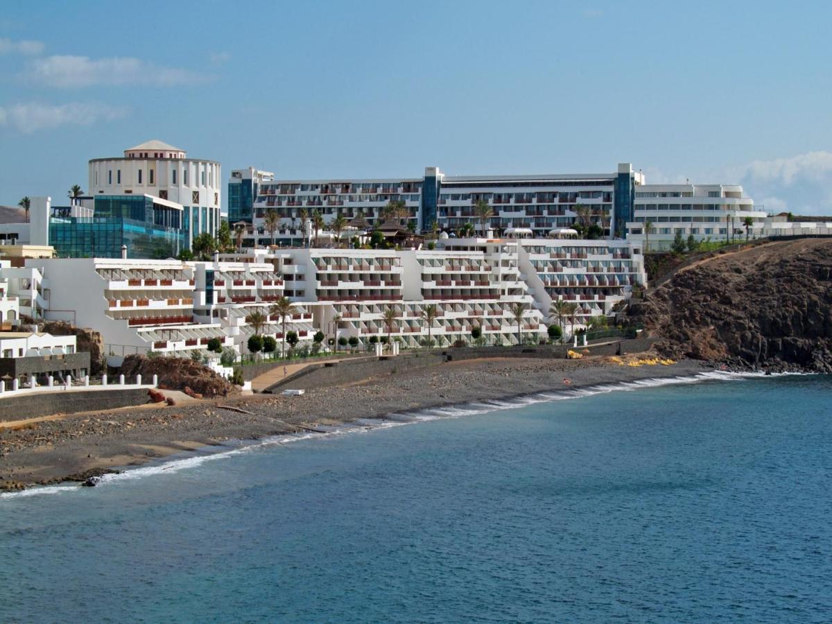 Un grupo de edificios blancos en una playa junto al agua. en Sandos Papagayo, en Playa Blanca