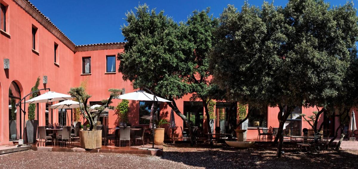un bâtiment avec des tables et des parasols devant lui dans l'établissement Hotel restaurant Spa Disini Montpellier Est, The Originals Relais, à Castries