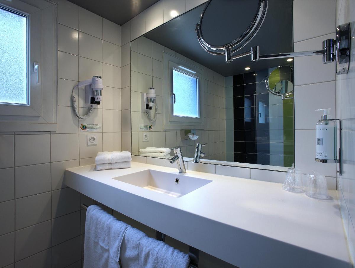 une salle de bains blanche avec un lavabo et un miroir dans l'établissement Hotel le Cinq Hyper - Centre, à Chambéry