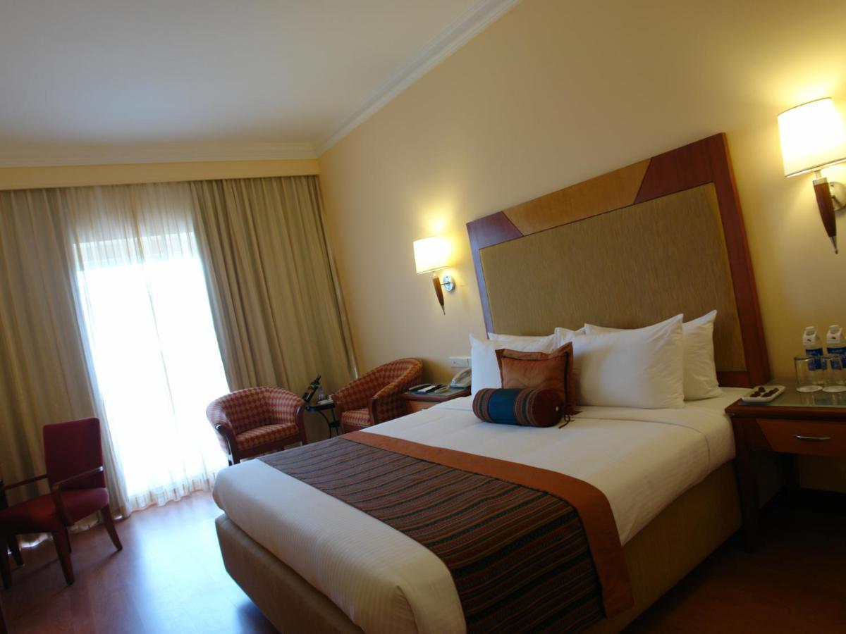 a hotel room with a large bed and a window at The Lalit Ashok in Bengaluru a hotel room with a large bed and a window at The Lalit Ashok in Bengaluru