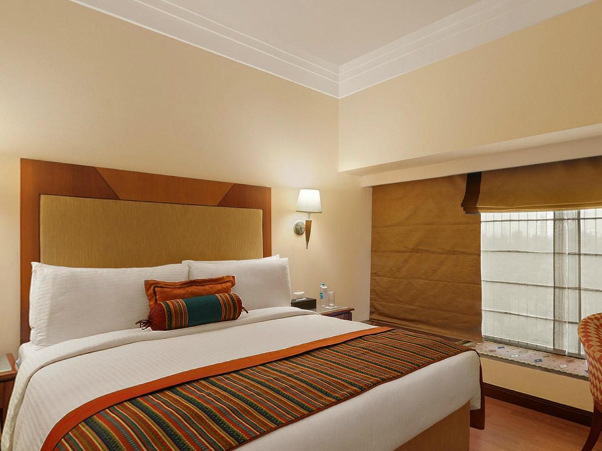 a bedroom with a large bed with a window at The Lalit Ashok in Bengaluru a bedroom with a large bed with a window at The Lalit Ashok in Bengaluru