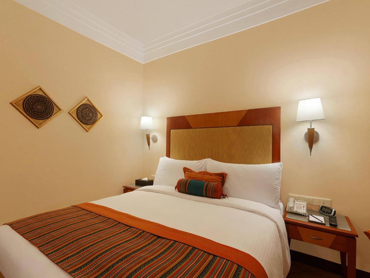 a hotel room with a large bed with white pillows at The Lalit Ashok in Bengaluru a hotel room with a large bed with white pillows at The Lalit Ashok in Bengaluru