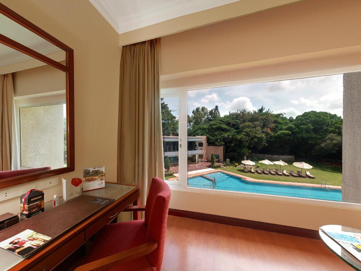 a room with a desk and a window with a view of a pool at The Lalit Ashok in Bengaluru a room with a desk and a window with a view of a pool at The Lalit Ashok in Bengaluru