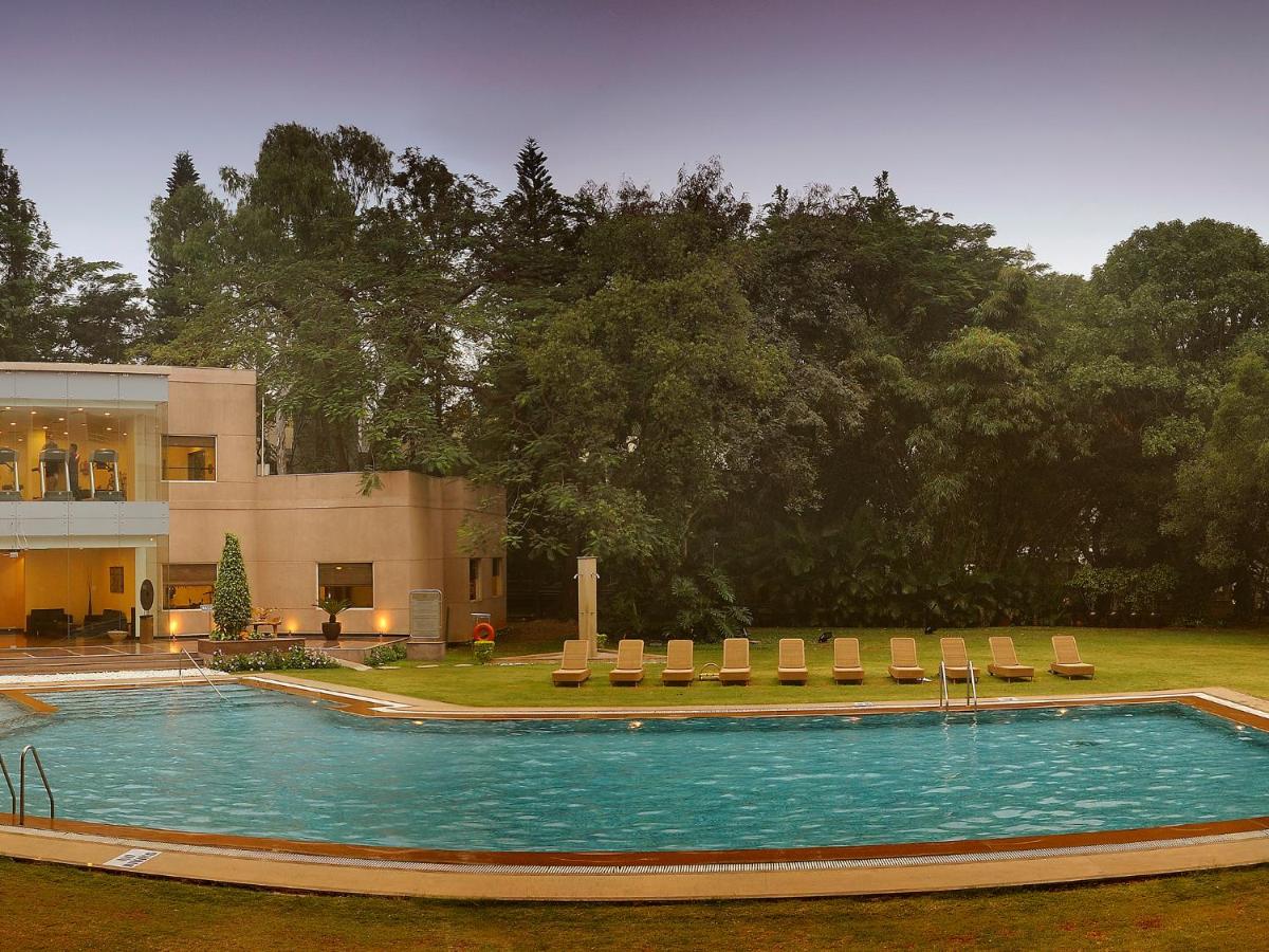 a large swimming pool with chairs and a building at The Lalit Ashok in Bengaluru a large swimming pool with chairs and a building at The Lalit Ashok in Bengaluru