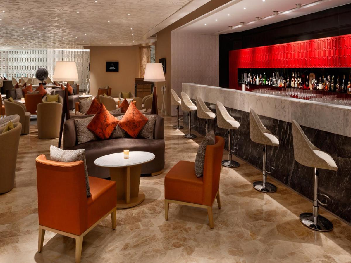 a lobby with a bar with couches and chairs at The Leela Ambience Convention Hotel Delhi in New Delhi