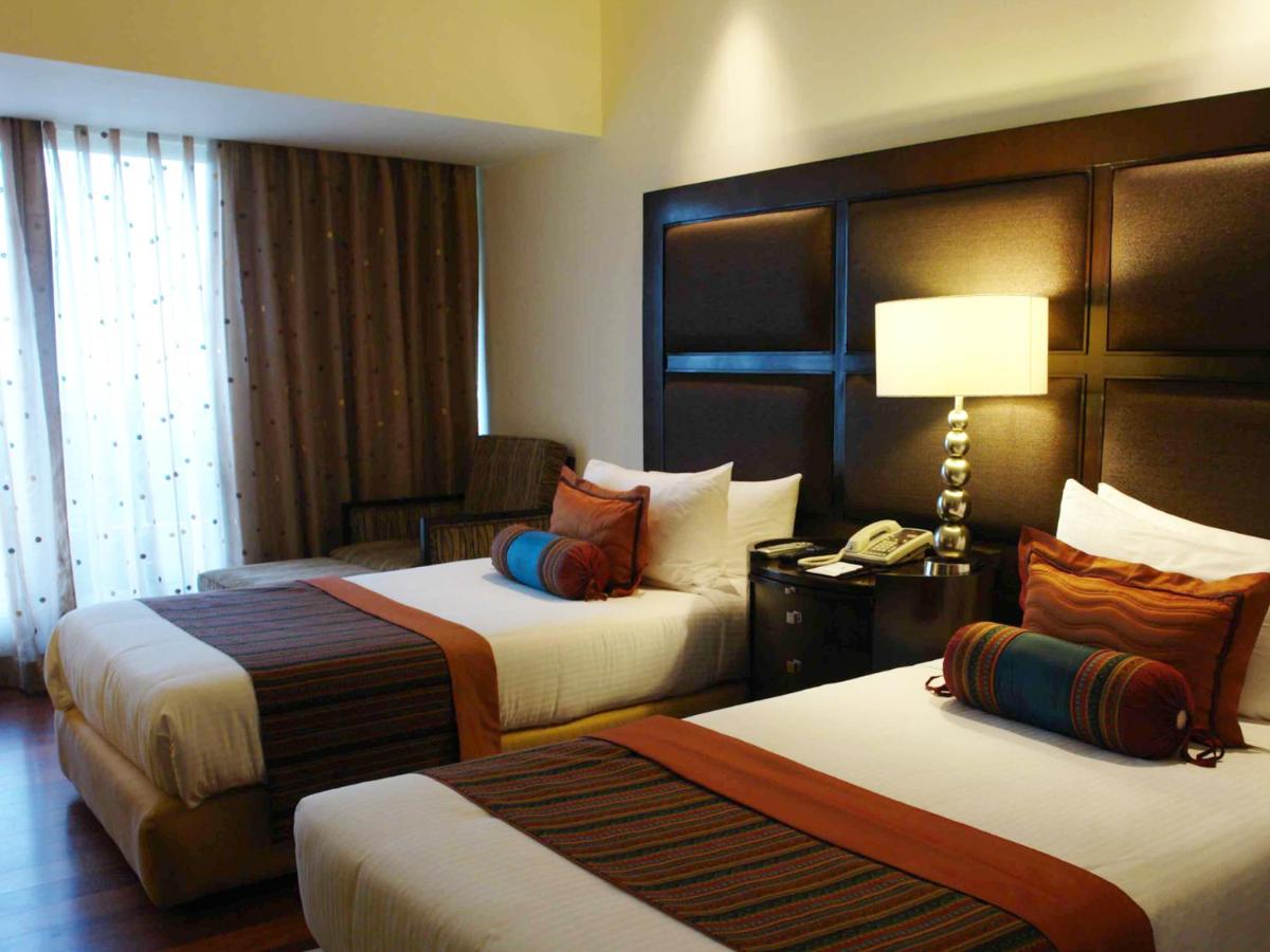 a hotel room with two beds and a chair at The Lalit Ashok in Bengaluru a hotel room with two beds and a chair at The Lalit Ashok in Bengaluru