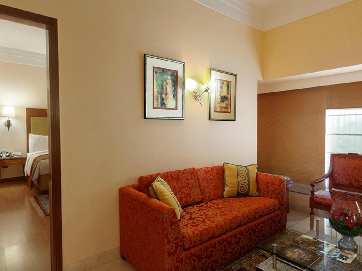 a living room with a red couch and a bedroom at The Lalit Ashok in Bengaluru a living room with a red couch and a bedroom at The Lalit Ashok in Bengaluru