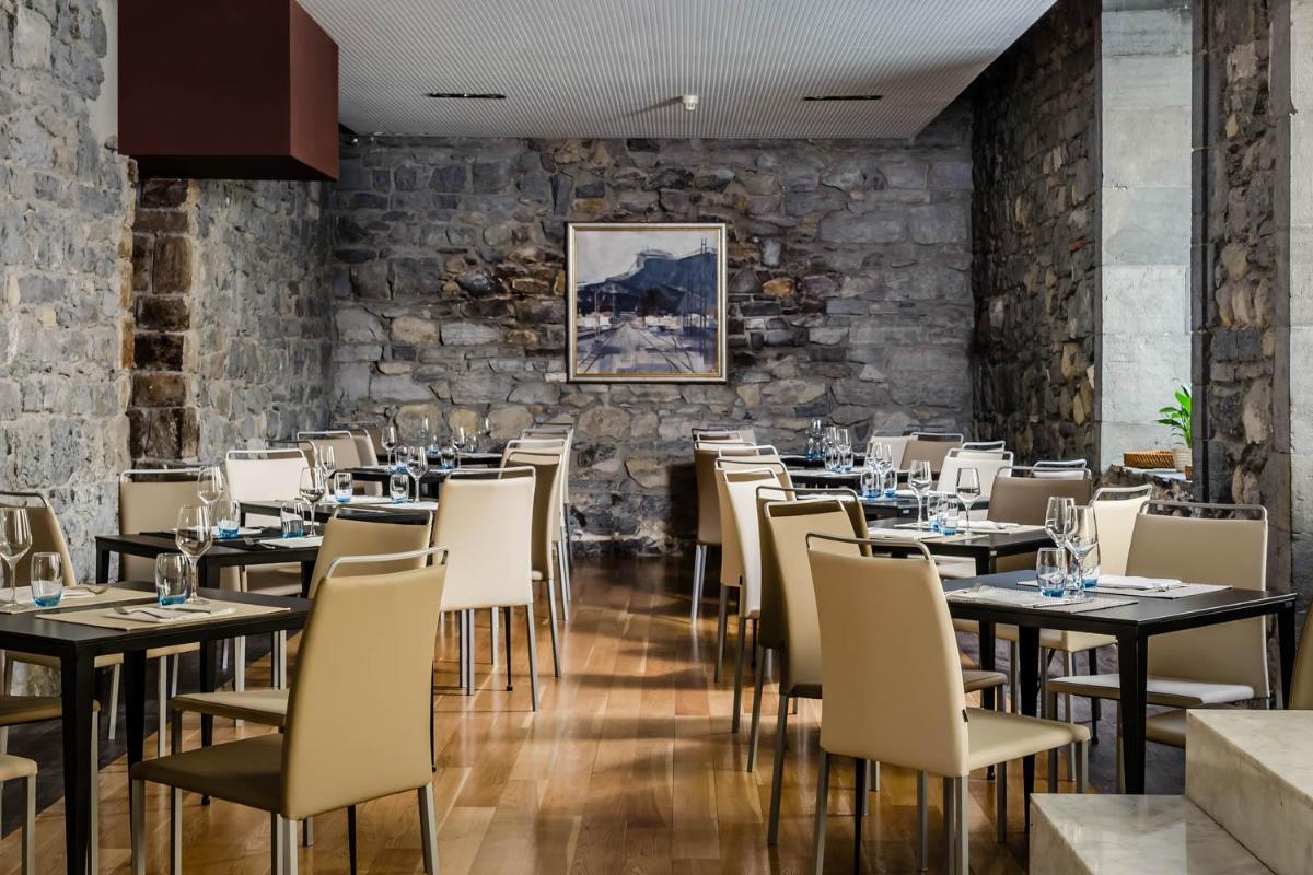 Un restaurante con mesas y sillas y una pared de piedra. en Hotel Balneario Orduña Plaza, en Orduña