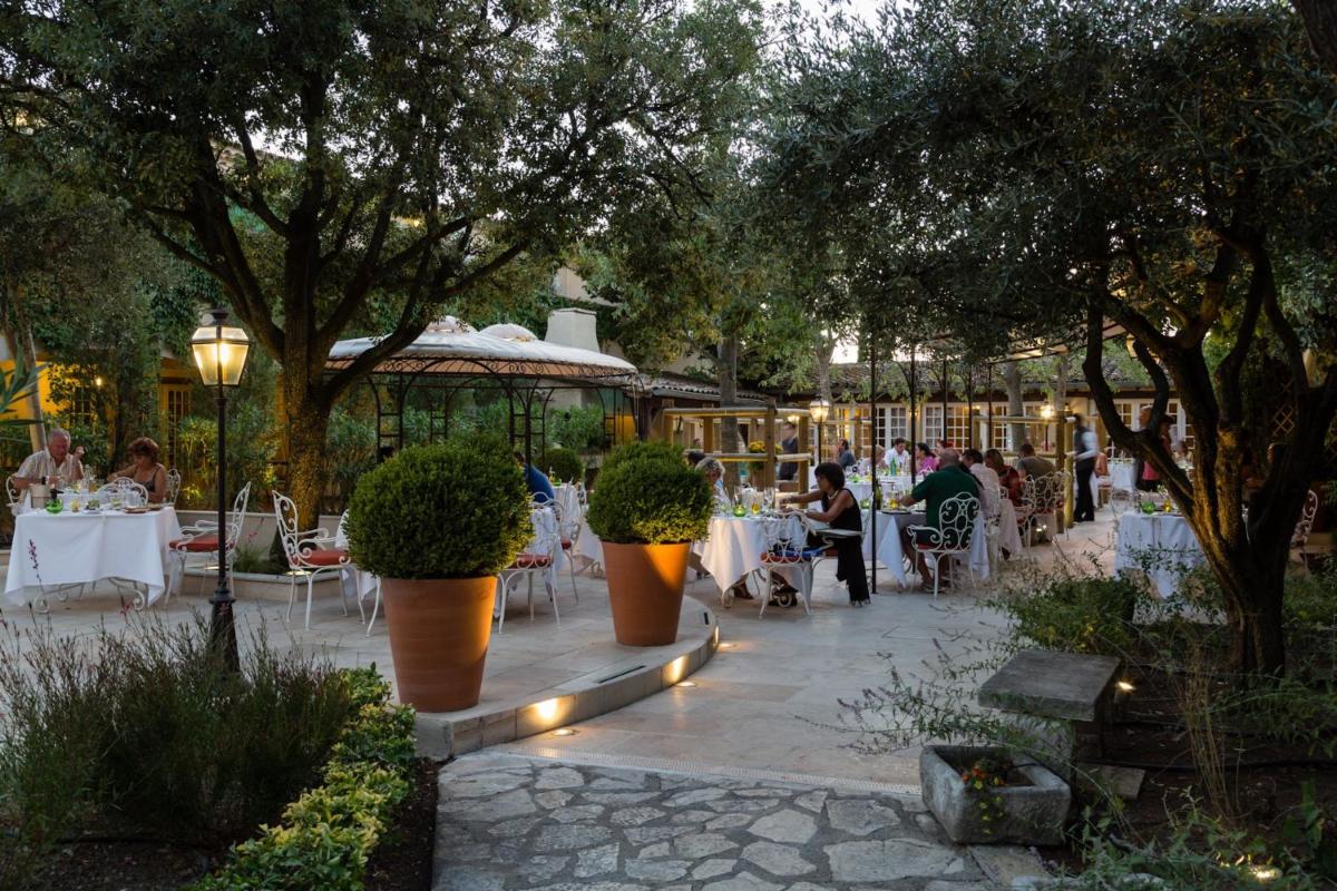 un patio avec des tables et des chaises et des personnes assises à des tables dans l'établissement Auberge de Cassagne & Spa, au Pontet