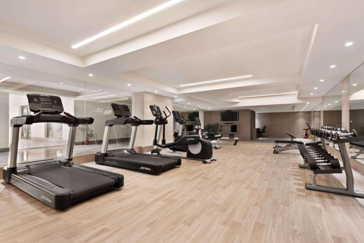 a gym with several treadmills and elliptical machines at Ramada by Wyndham Lucknow Hotel and Convention Center in Lucknow