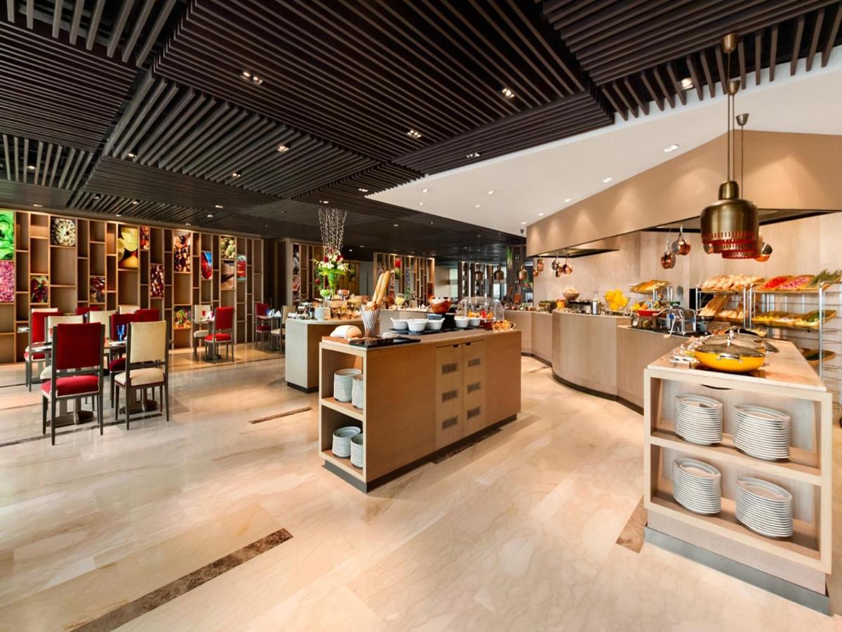 a restaurant with a buffet line with tables and chairs at The Leela Ambience Convention Hotel Delhi in New Delhi