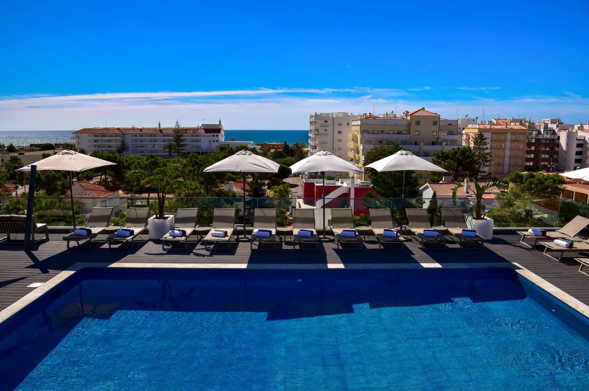 uma piscina com cadeiras e guarda-sóis em The Prime Energize Hotel & SPA - Algarve em Monte Gordo